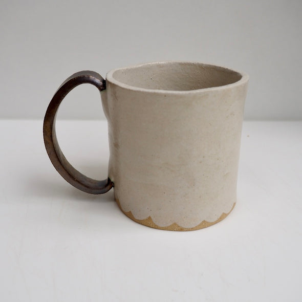 Cream ceramic mug with a scalloped lower edge and a gold handle