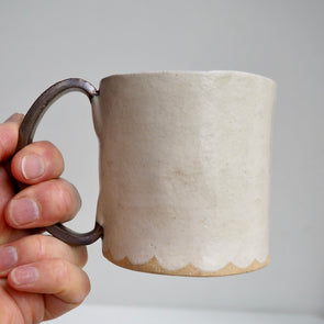 Cream ceramic mug with a scalloped lower edge and a gold handle