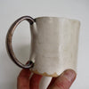 Cream ceramic mug with a scalloped lower edge and a gold handle