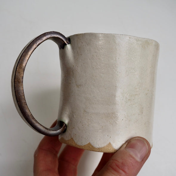 Cream ceramic mug with a scalloped lower edge and a gold handle