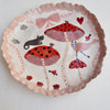 Handmade illustrated plate with toadstools, cat, hearts, and bows.