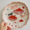 Handmade illustrated plate with toadstools, cat, hearts, and bows.