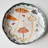 Handmade illustrated plate with toadstools, swan, lion, snake and clouds.