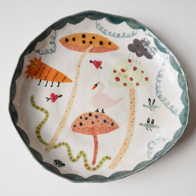 Handmade illustrated plate with toadstools, swan, lion, snake and clouds.