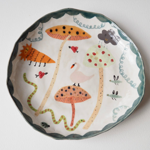 Handmade illustrated plate with toadstools, swan, lion, snake and clouds.